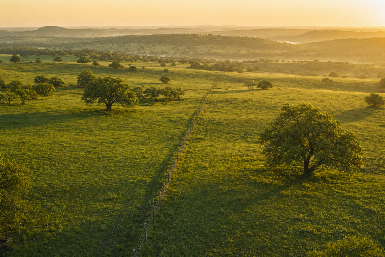 Aerial view of a fence line crossing open rangeland at dawn.